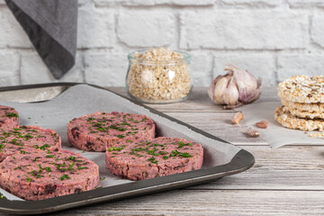 Raw veggie burger with beetroot and white beans with parsley leaves on wood cutting board.