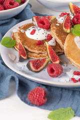 Pancakes with raspberries, figs, yogurt, coconut zest, honey and mint leaves on a plate.