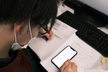 スマホで調べ物（勉強）をするマスク姿の大学院生