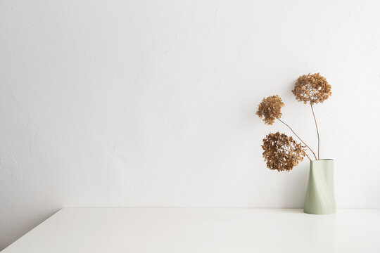 White desk with  minimal vase with a decorative dried branches against white wall.