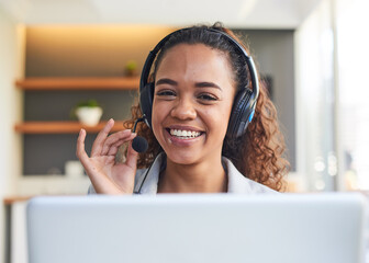 A centred view of a young woman behind her laptop with headset in modern office