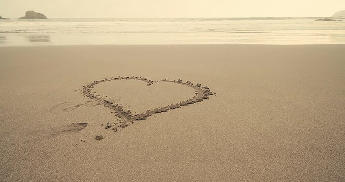 The beach drawing hearts on a sand on seashore out with waves on background, summer vacation, Romantic composition.