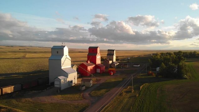 Aerial rotating shot of three Grain Elevators surrounded by agricultural fields in southern Alberta, Canada at sunset.