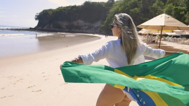 latin woman with brazil flag celebrating, in a beach setting. Large northern river. Madeiro Beach. Supporter of the Brazilian team.