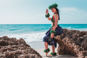 Hawaii dancer smiling woman on the beach showing her hands waving saying hello. Hawaiian woman waves to the camera and smiles relaxed on rocky beach. Oriental and exotic beauty. Hula dancer hawaii.