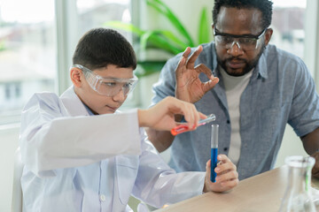 Boy student scientist wearing protection glasses studying chemistry and making experiments in tubes in elementary science class with his teacher.Education and Science