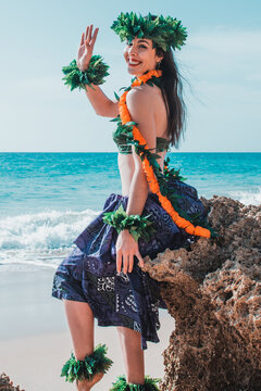 Waving hand girl. Lady waves her hand. Smiling hula dancer says hello to welcome. Hawaiian woman waves to the camera and smiles relaxed on a paradisiacal beach. Oriental and exotic beauty.