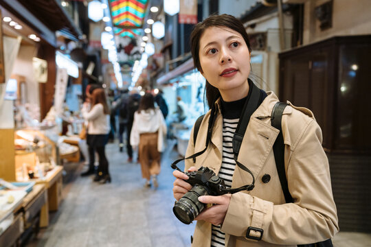 korean girl just spot something interesting in Kyoto's traditional market and took her camera up. woman tourist looking into distance with camera is thinking what photo to take in Nishiki market