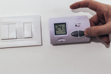 Close up view of a hand adjusting the heating temperature. Digital thermostat on the wall of the...