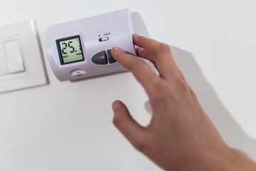 Close up view of a hand adjusting the heating temperature. Digital thermostat on the wall of the house