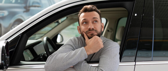A man sits inside a car thinking about buying on credit at a car dealership