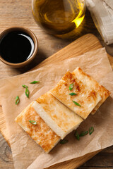 Fototapeta na wymiar Delicious turnip cake with green onion and soy sauce on wooden table, flat lay