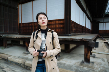 asian woman photographer standing by japanese old construction notices something in distance....