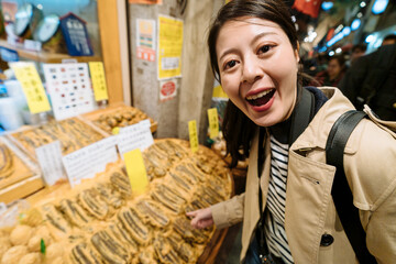 travel tv series hostess pointing at preserved radish in market is introducing special japanese cuisine to audience. female tourist looking at camera is amazed at a traditional japanese food.