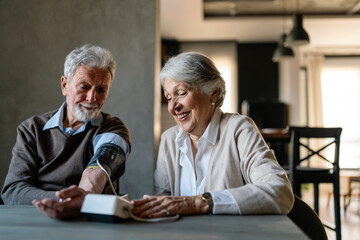 Happy senior couple measuring blood pressure at home