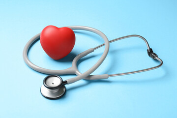 Stethoscope and red decorative heart on light blue background. Cardiology concept