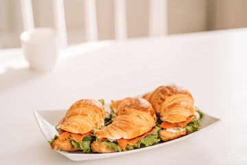Croissants with red fish lie on square plate.