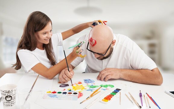Painting concept. Schoolgirl painting with father during therapy at home with his tutor with learning and having fun together.