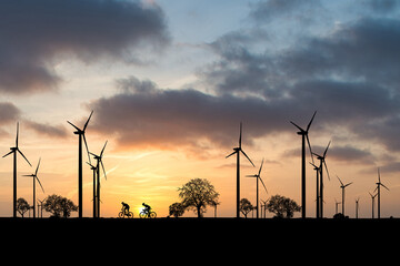 Clean energy concept. Cyclists in a beautiful windmill field producing electricity.