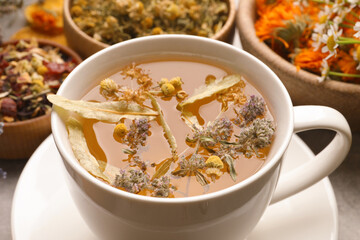 Cup of aromatic freshly brewed tea and different dry herbs on table, closeup