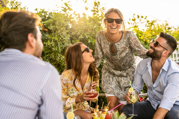young group of 30s people having fun at a cocktail party outdoor, beautiful women smiling and laughing with friends, handsome men talking with elegant female millenials - Powered by Adobe