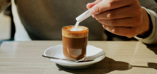 man ads some sugar to his machiatto, banner format