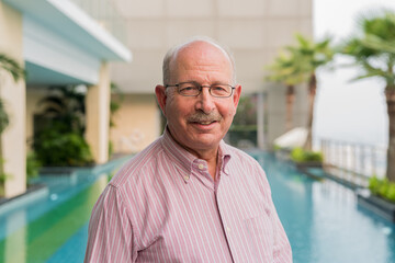 Portrait of senior man smiling next to swimming pool outdoors - 491647449