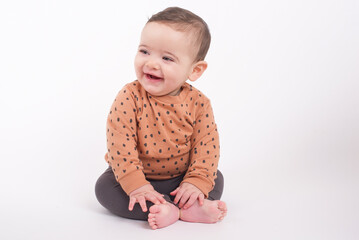 Adorable baby boy wearing animal print sweater and grey pants sitting on white background looking aside and smiling to his mom. 