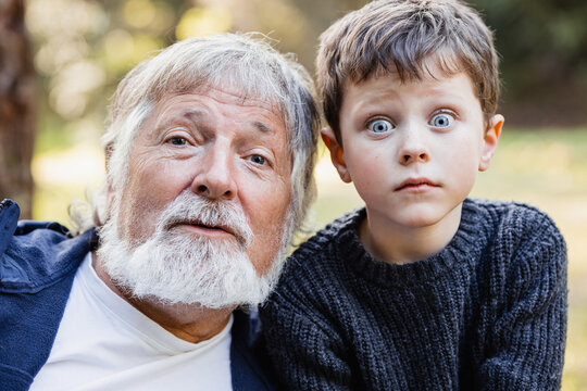 Positive senior grandfather looking at camera and grandson goggle eyes