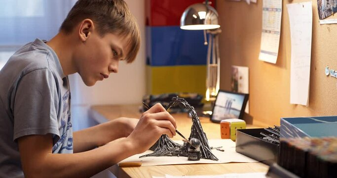 Teenage boy painting board game model. Sitting in his room