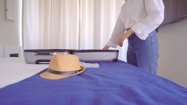 a young beautiful woman in a white shirt and jeans takes things out of a suitcase upon arrival on vacation or after vacation. . With a smile on her face, she is going to rest. Apartment or hotel room.
