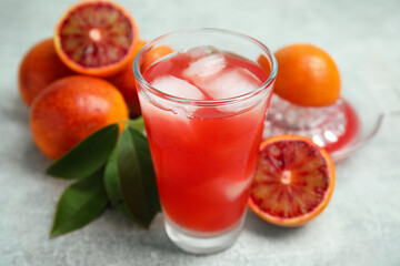 Tasty sicilian orange juice with ice cubes in glass and fruits on light grey table, closeup