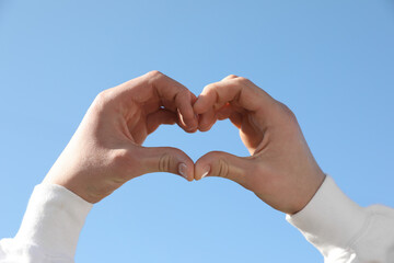 Man showing heart against blue sky outdoors on sunny day, closeup of hands