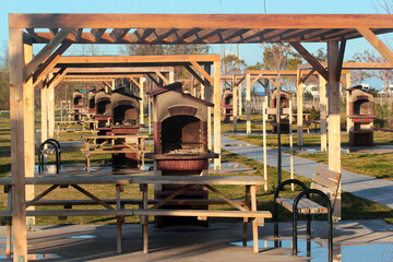 Wooden arbors with tables benches and barbeque equipment in a public park