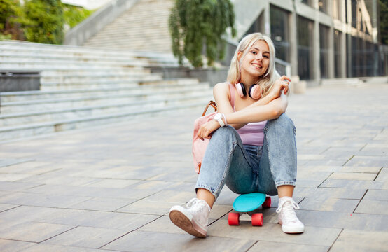 Young smiling cool girl sitting on skateboard in the city