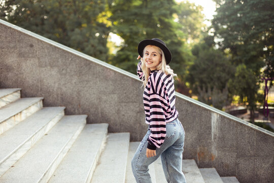 Young charming hipster girl in hat walking up the stairs outdoors