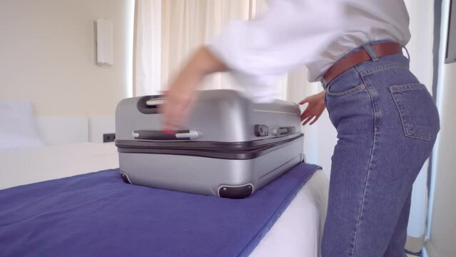 a young beautiful woman in a white shirt and jeans takes things out of a suitcase upon arrival on vacation or after vacation. . With a smile on her face, she is going to rest. Apartment or hotel room.