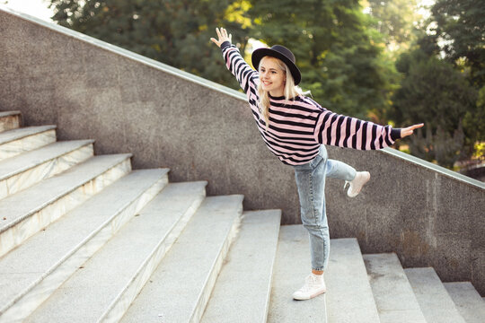 Young charming hipster girl in hat having fun on stairs outdoors
