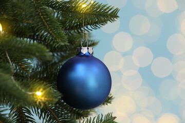 Fototapeta na wymiar Beautiful blue bauble hanging on Christmas tree against blurred festive lights, closeup