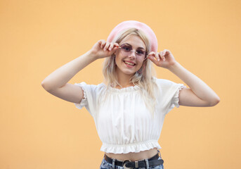 Emotional smiling girl in a beret and sunglasses having fun on yellow background. Portrait of cool hipster woman in trendy outfit. Lifestyle