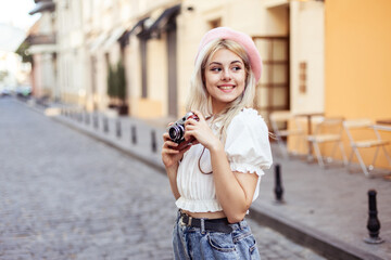 Charming hipster girl in beret with retro camera in city. Travel concept, lifestyle. French style