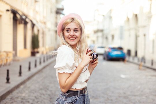 Charming hipster girl in beret with retro camera in city. Travel concept, lifestyle. French style