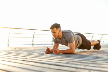 Athletic man in sportswear practicing plank on the beach in the early morning