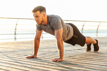 Naklejka premium Athletic man in sportswear practicing push-ups on the beach in the early morning