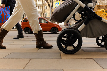 Stylish woman walks with stroller, goes from store with purchases, red car drives by, busy traffic on sidewalk