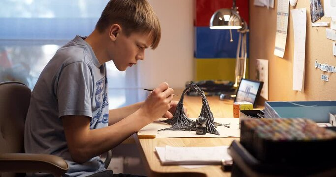Teenage boy painting board game model. Sitting in his room
