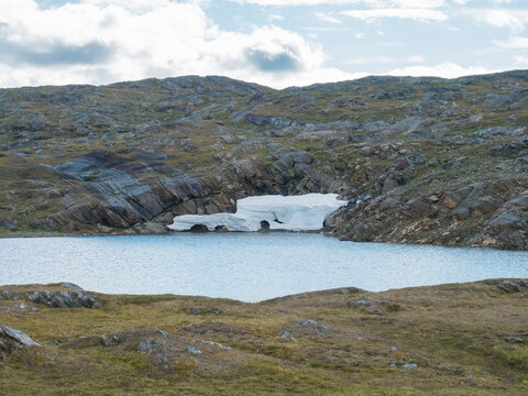 Northern Landscape, Tundra In Swedish Lapland With Blue Artic Lake With Reamains Of Melting Snow Cave, Green Hills And Mountains At Padjelantaleden Hiking Trail. Summer Day, Blue Sky, White Clouds