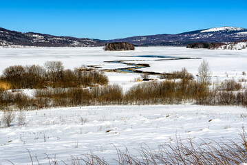 Obraz premium Winter landscape by the frozen lake with hills in the background background. Frozen Lake on a cold winter day