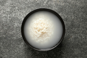 Bowl with rice soaked in water on grey table, top view