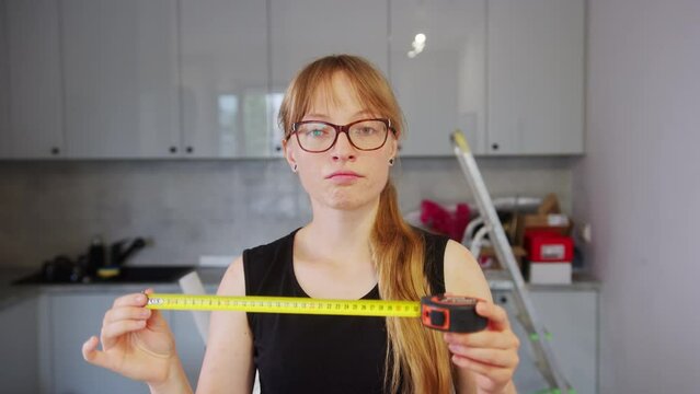 Beautiful woman carpenter using measure tape in his kitchen. Showing measure tape in front of the camera